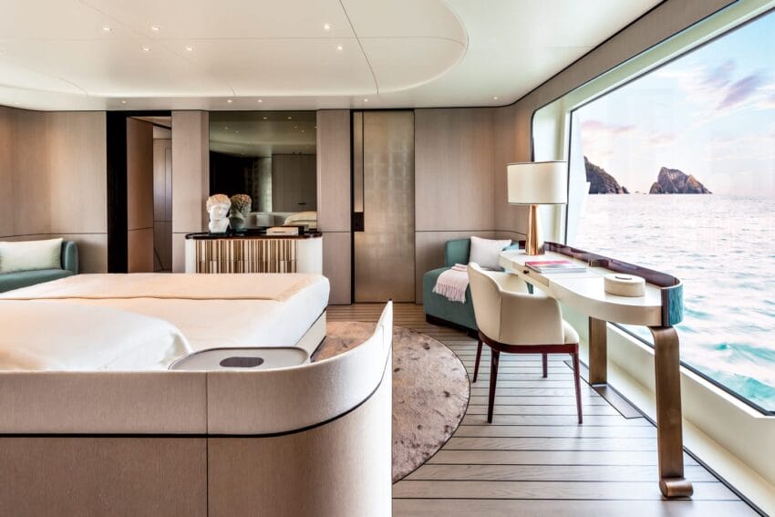 Luxurious yacht bedroom with modern furnishings, large window view of ocean and cliffs, soft lighting, and elegant decor.