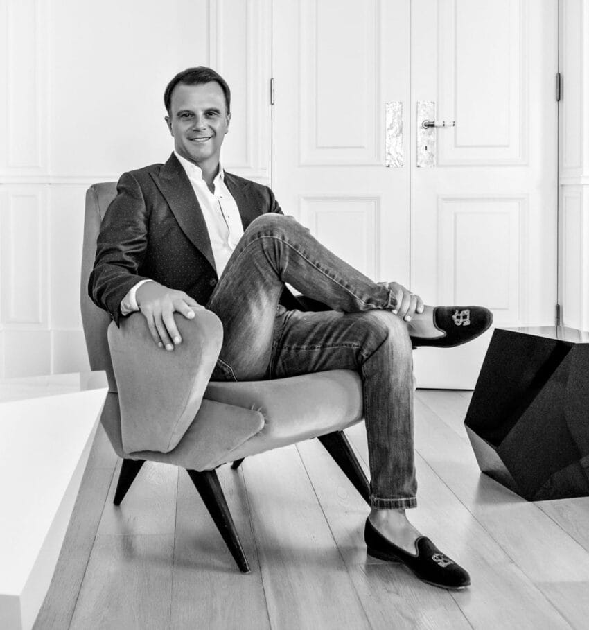 Smiling person seated in a modern armchair in a stylish room with a geometric black table and wooden floor.