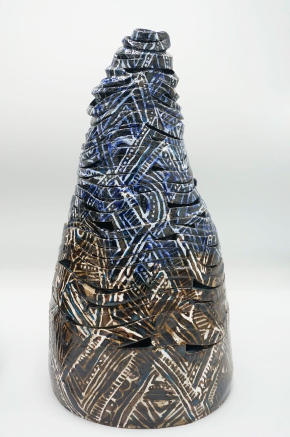 Ceramic sculpture with intricate blue and brown patterns on a white background, resembling a textured, abstract cone shape.
