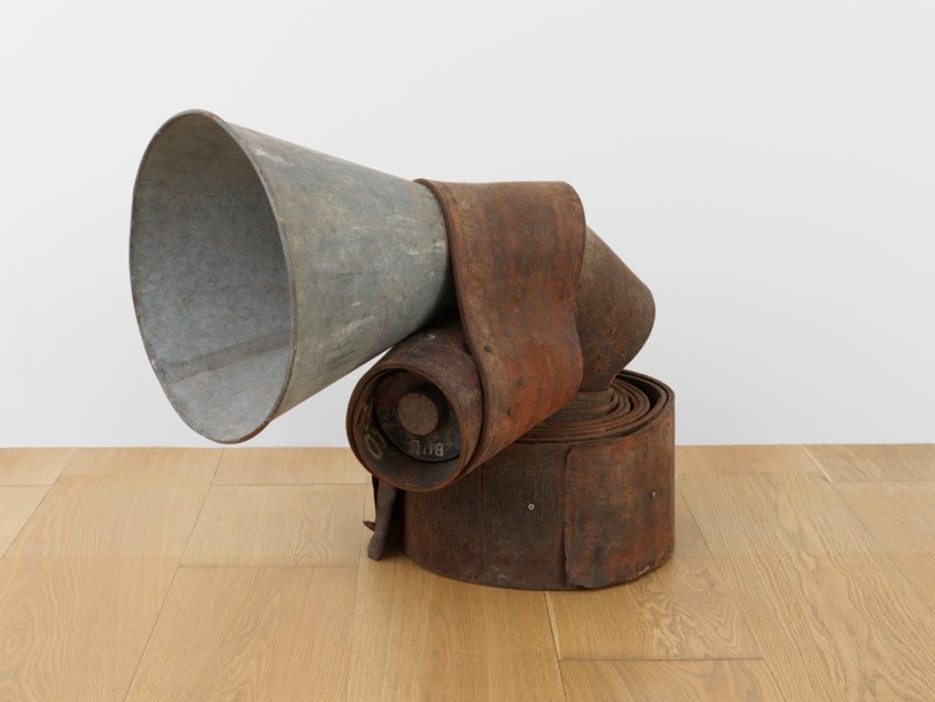Rustic metal and leather sculpture resembling a large horn, displayed on a wooden floor.