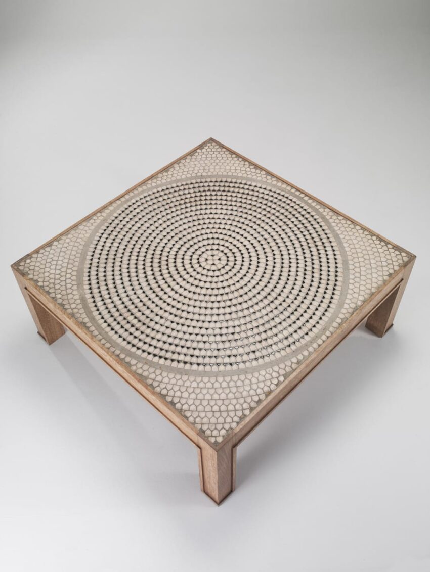 Square wooden table with a decorative circular pattern on the surface, viewed from above on a plain background.