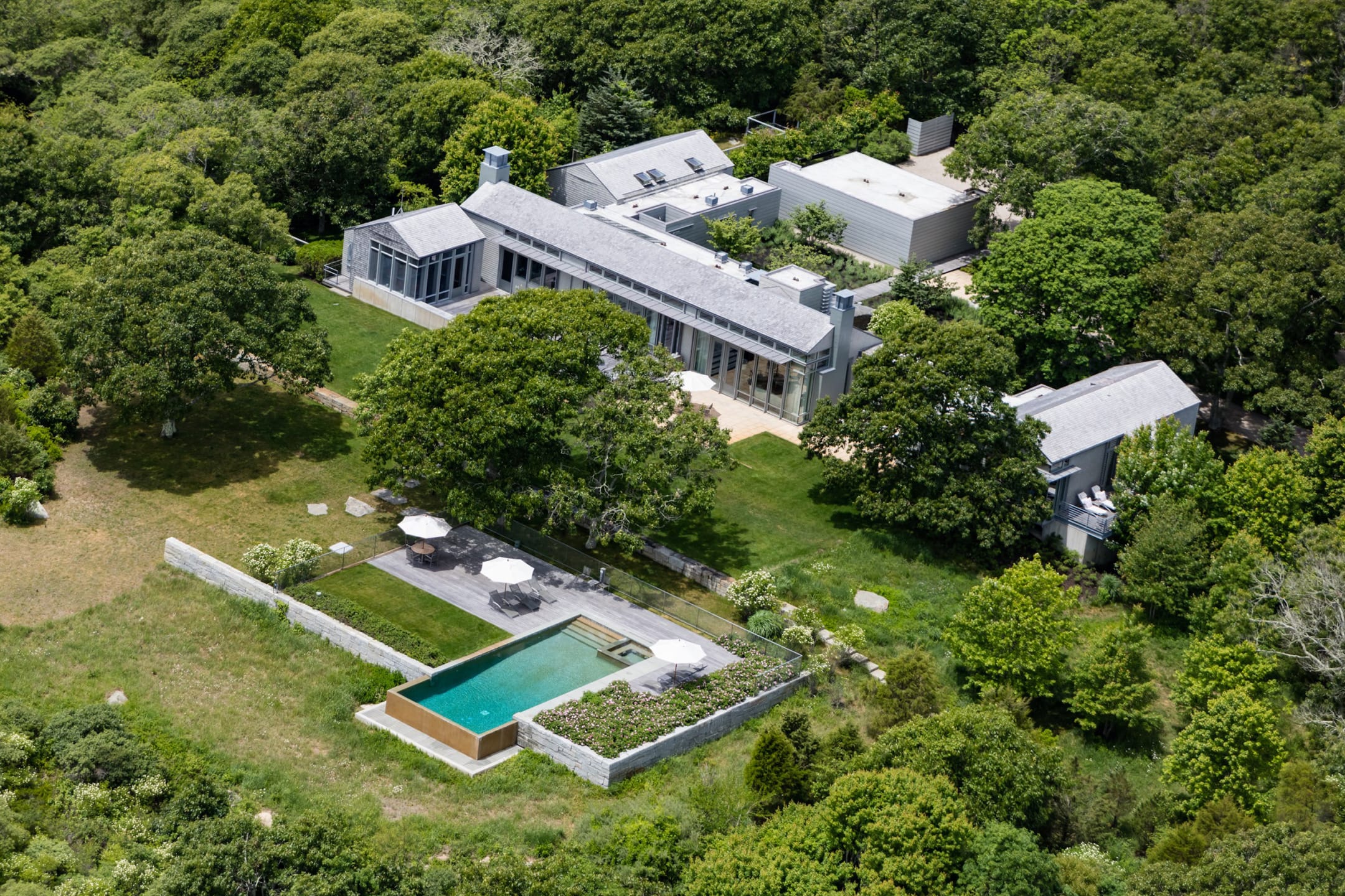 Aerial view of a modern house surrounded by trees with a swimming pool in the foreground.