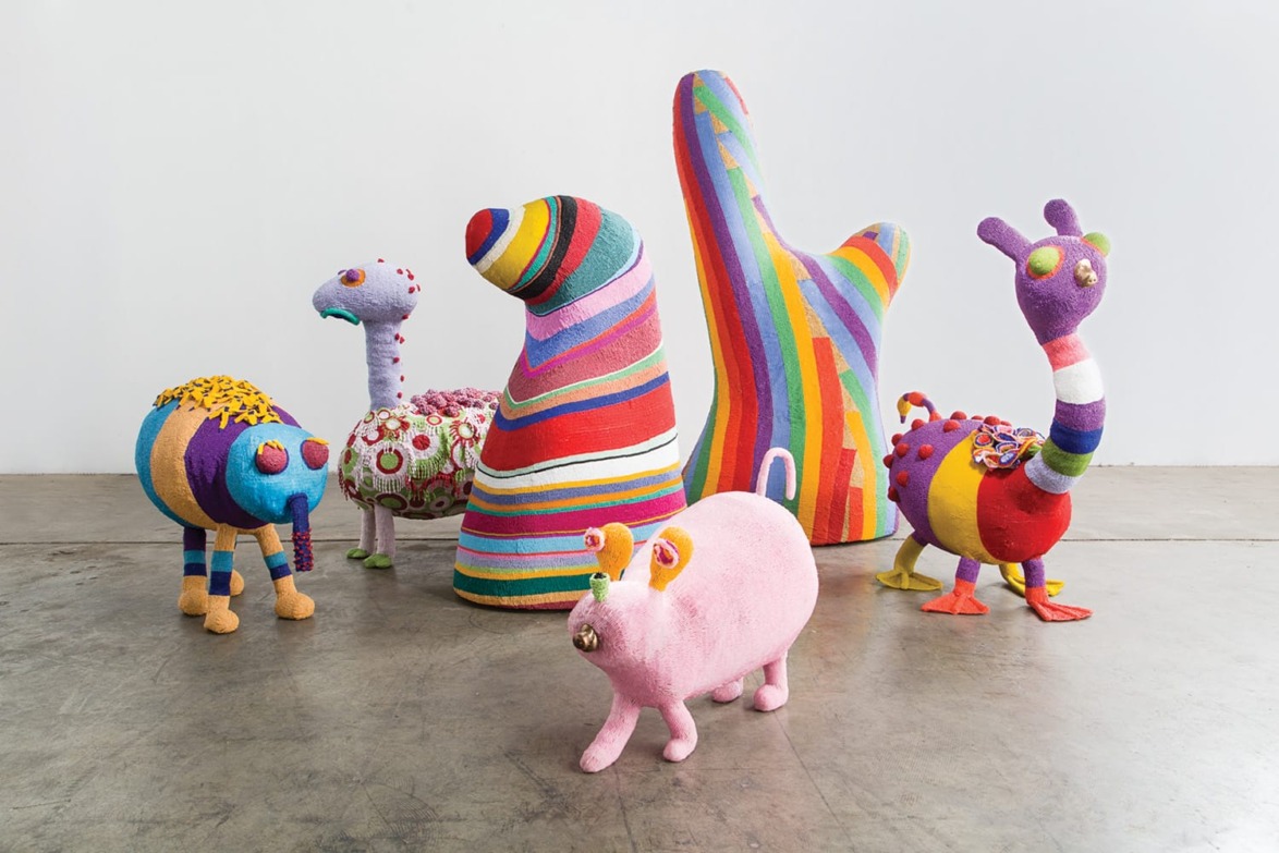 Colorful, whimsical yarn sculptures resembling imaginative creatures displayed on a concrete floor.