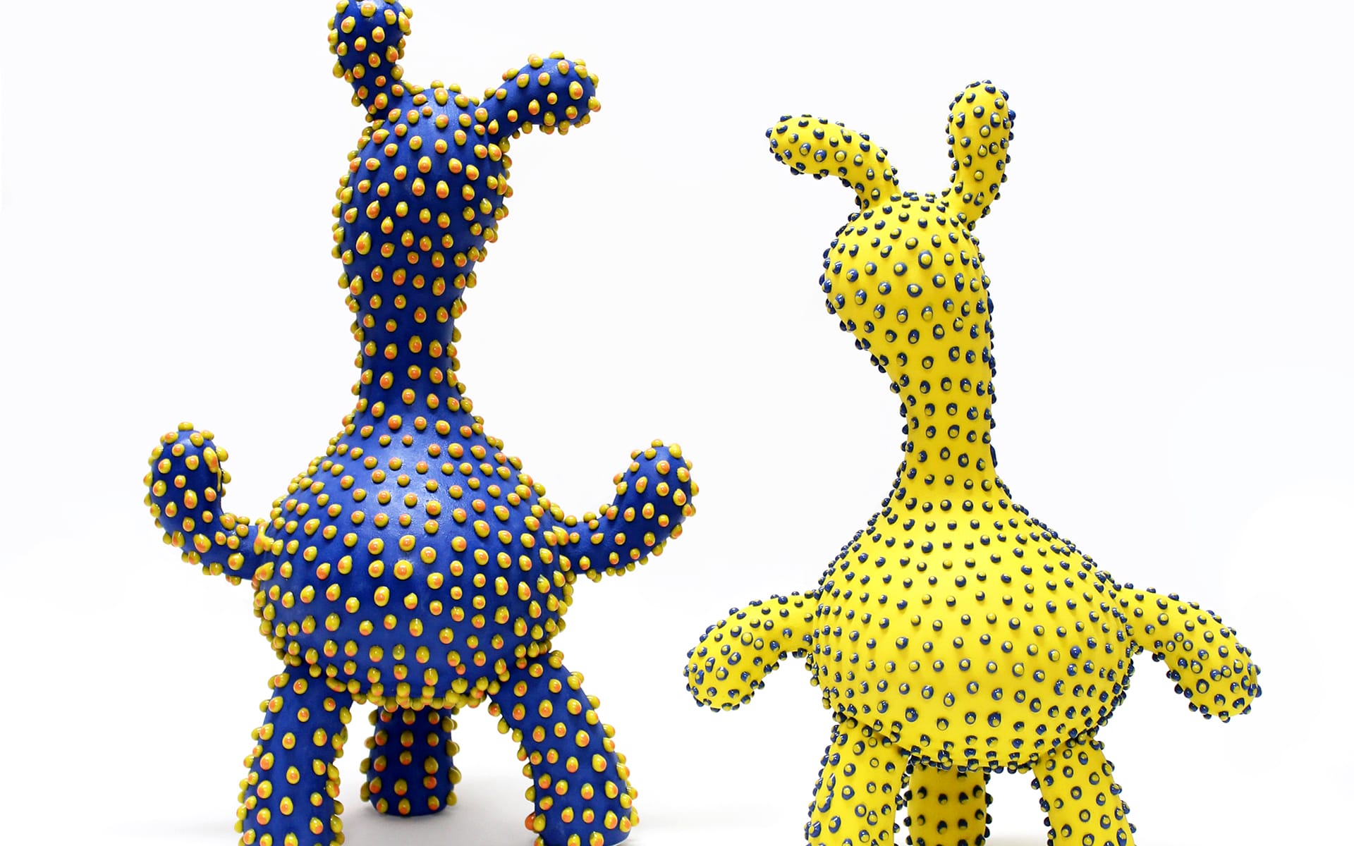 Two colorful abstract sculptures with small protrusions, one blue and one yellow, against a white background.