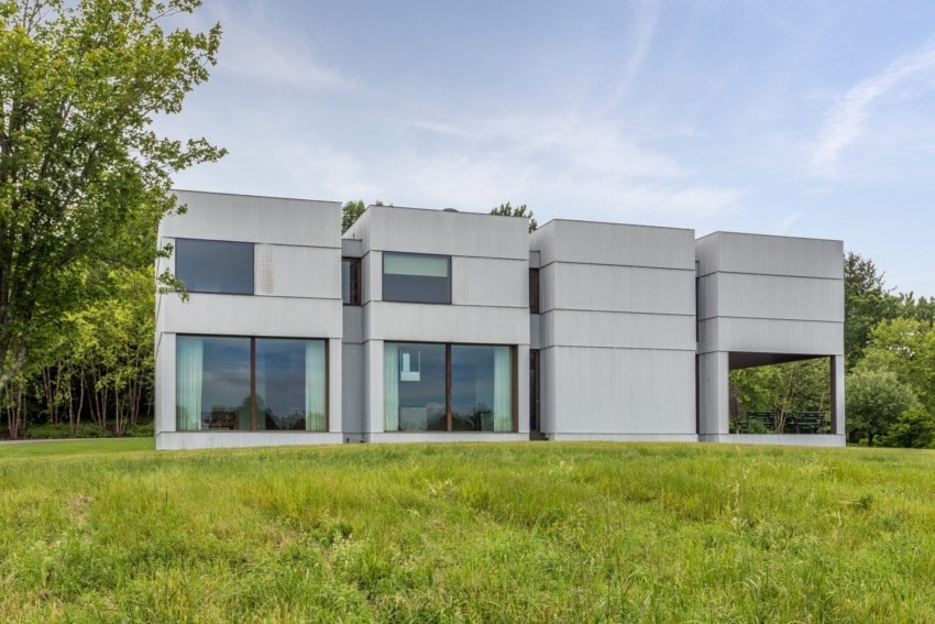 Modern minimalist house with large windows surrounded by greenery and a clear blue sky in the background