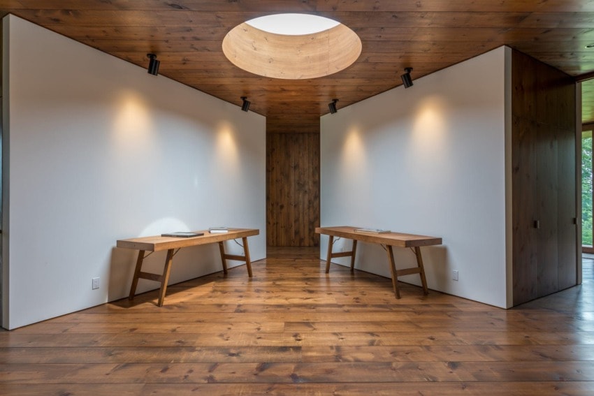 Minimalist room with wooden floors, two wooden benches, white walls, and ceiling spotlight.