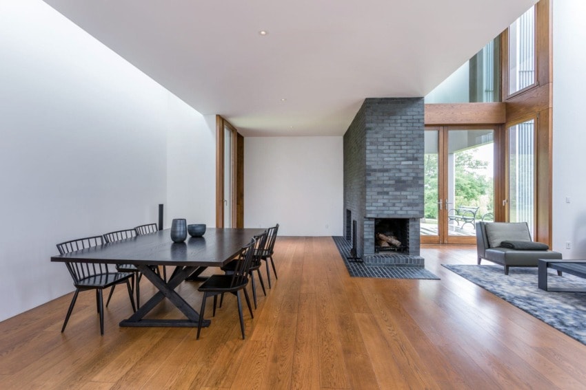 Modern dining room with wooden floor, black table, chairs, large fireplace, and tall windows bringing in natural light.