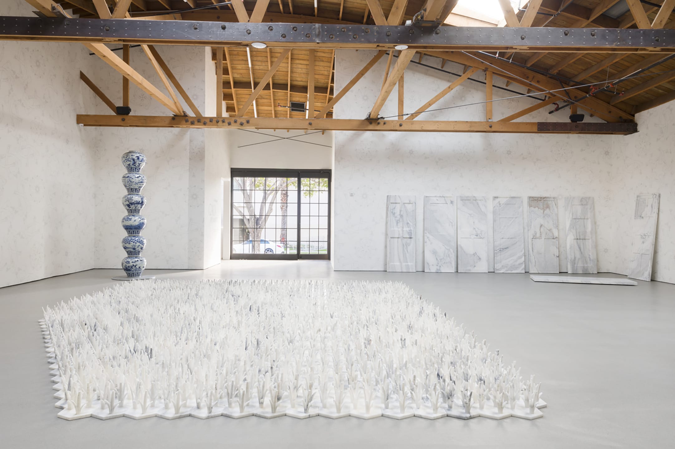 Contemporary art installation in a bright gallery with wooden beams featuring porcelain and textured sculptures.