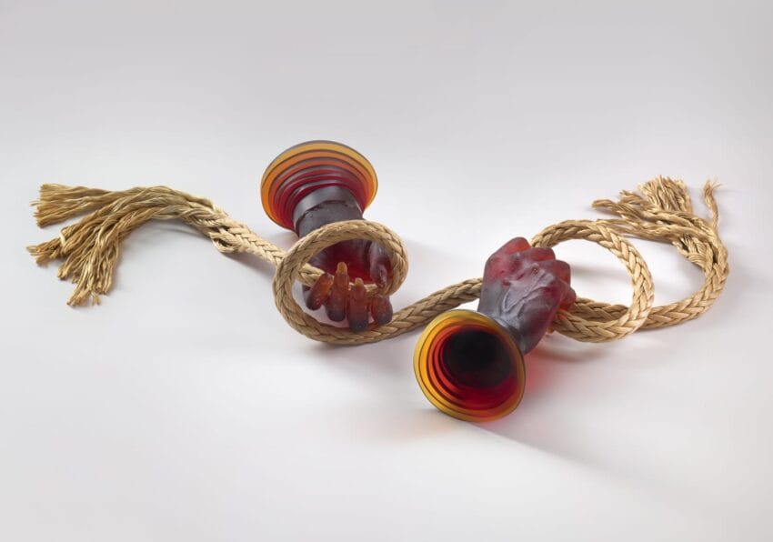 Colorful glass candlestick holders entwined with detailed braided rope on a plain background.