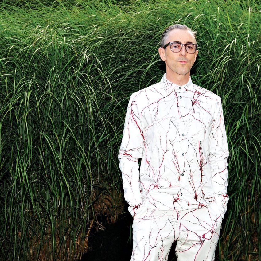 Person in a white suit with red patterns standing in front of tall grass.