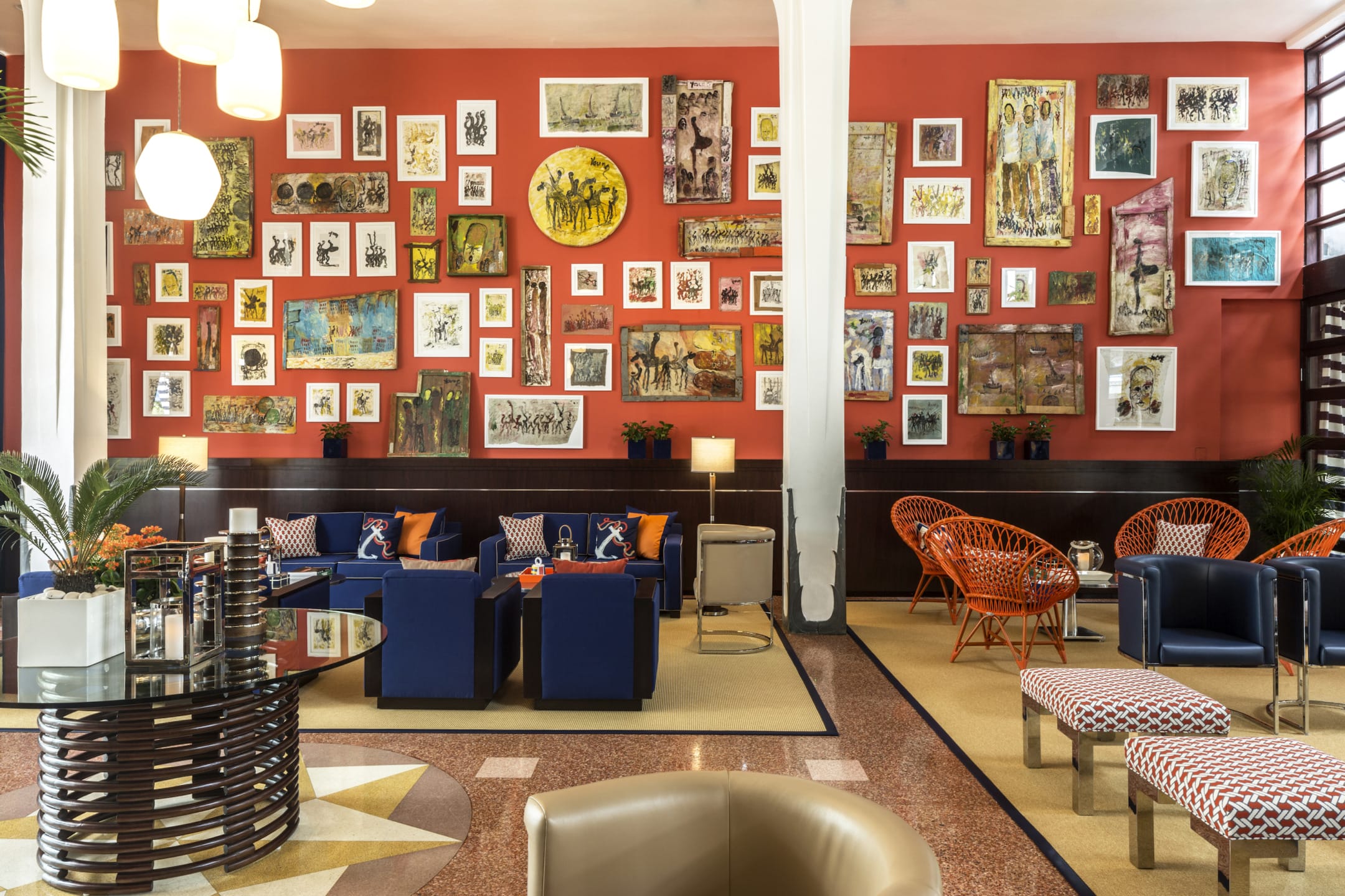 Stylish hotel lobby with vibrant red walls, eclectic art gallery display, blue seating, and orange accent chairs.