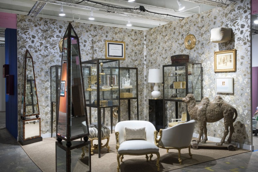 Antique shop display with elegant furniture, mirrors, and decorative items against a floral patterned wallpaper background.