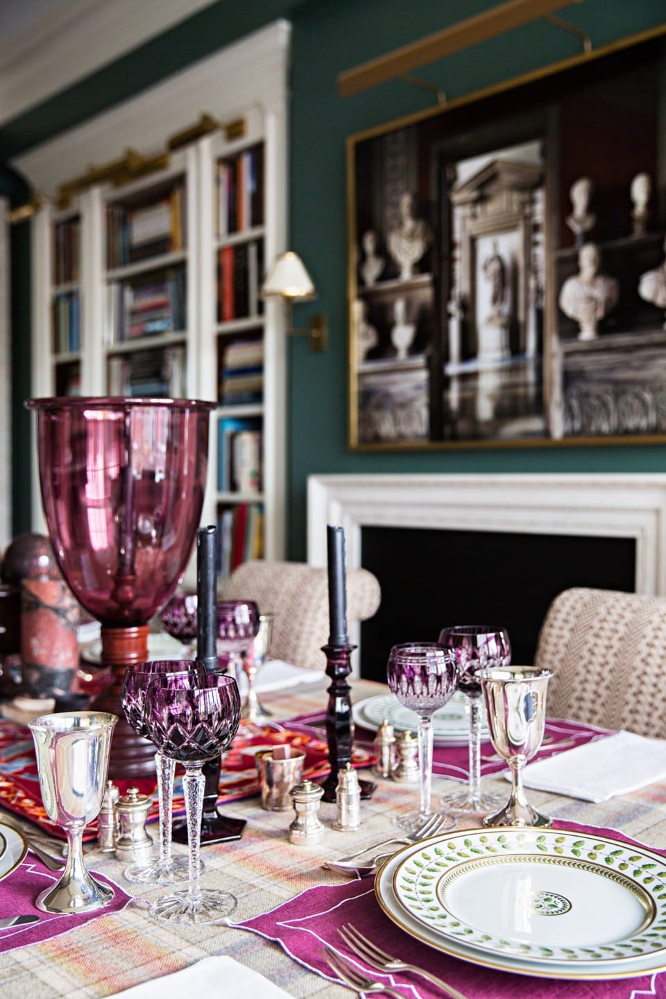 Elegant dining table setting with purple glassware, silver accents, patterned plates, and decorative furniture in the background.