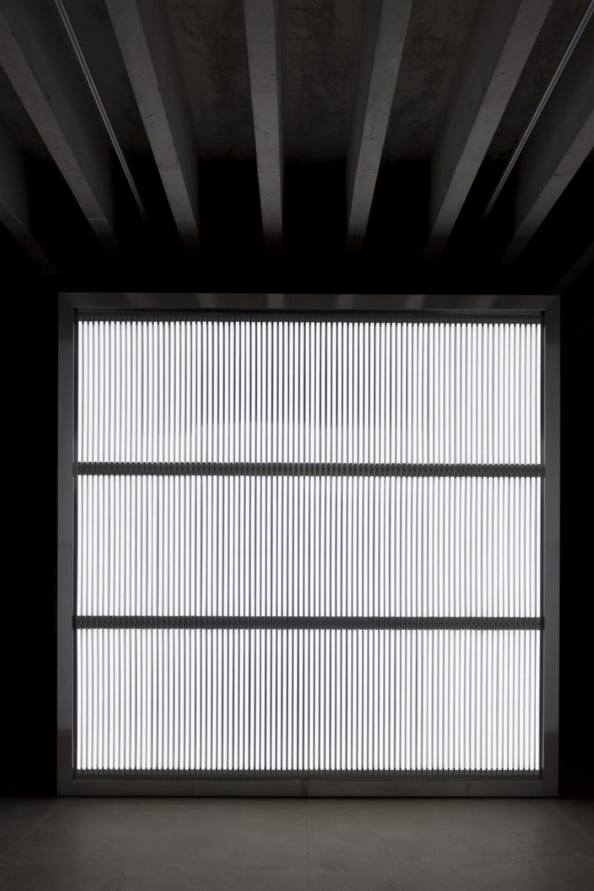 Illuminated vertical light stripes in a dark room with concrete ceiling and floor, creating a modern geometric pattern.