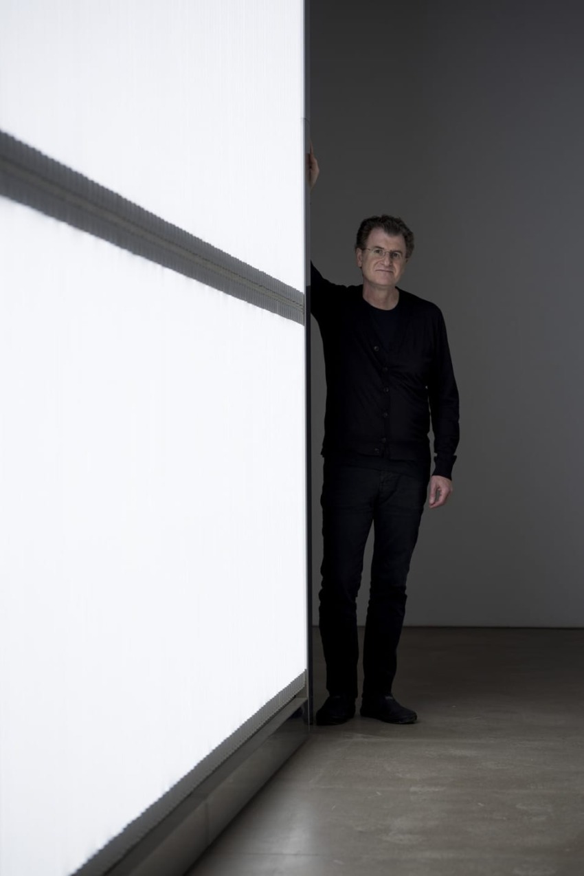 Man in dark clothing standing beside a large illuminated panel in a dimly lit room.