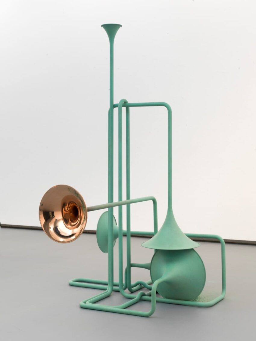 Sculptural artwork featuring abstract musical instrument shapes in pastel green with a metallic horn on a gray floor.