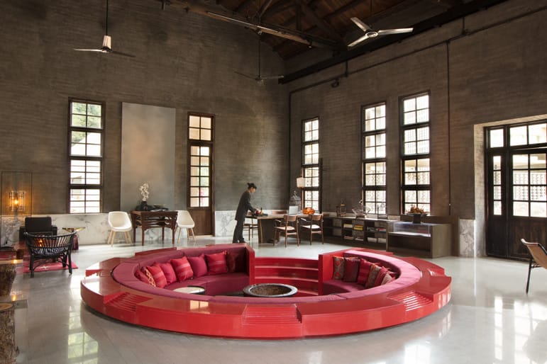 Spacious living room with red circular seating area, high ceilings, and large windows. Person standing at a desk.