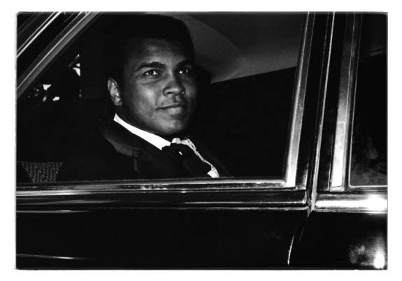 Man seated inside a car, gazing out of the window with a calm expression, dressed in formal attire.