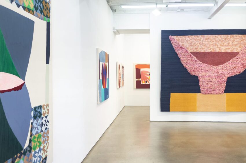 Contemporary art gallery with abstract paintings on white walls, showcasing vibrant colors and geometric patterns.