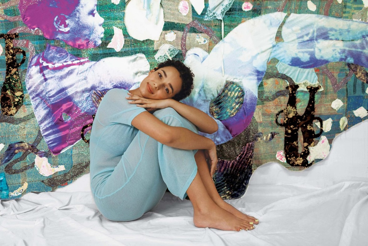 Woman in blue outfit sitting against a colorful abstract background, resting her chin on her arms, with a thoughtful expression.