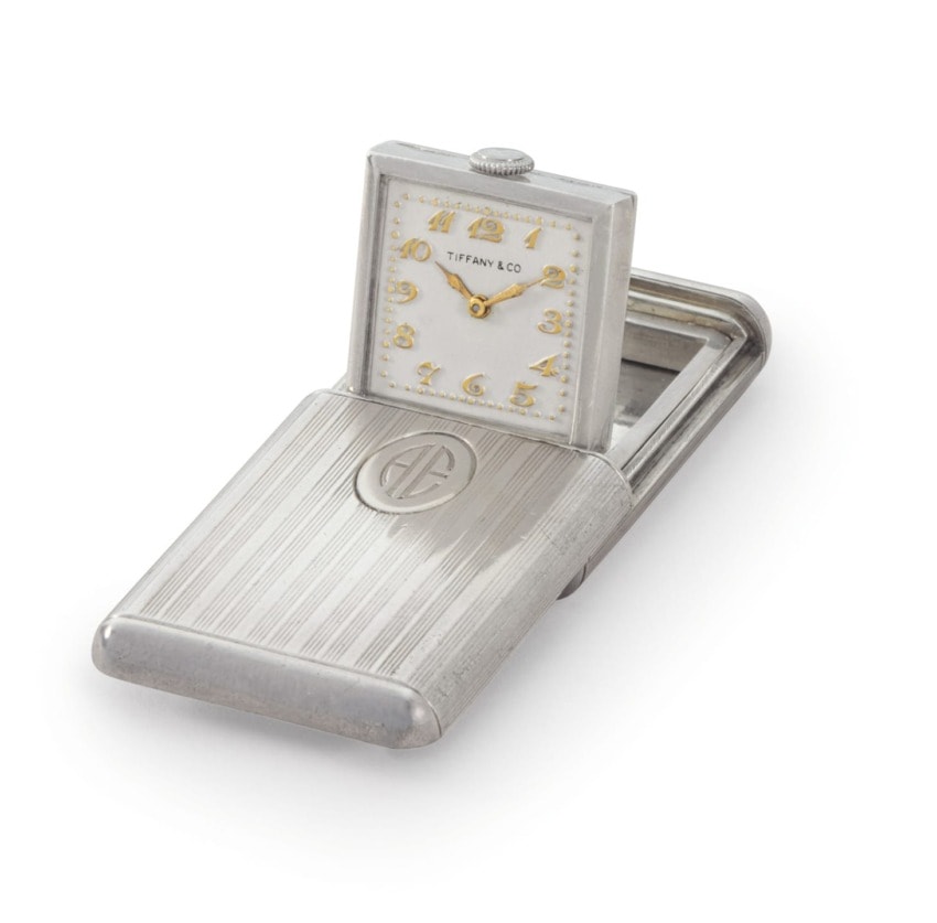 Vintage Tiffany & Co. travel alarm clock with silver case, displaying time on an engraved cover, viewed from an angle.