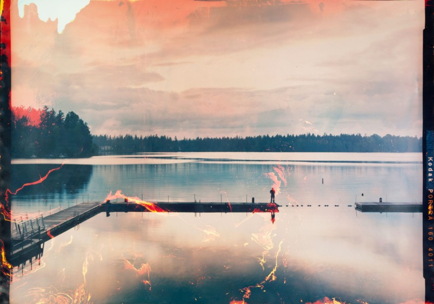 A serene lake with a wooden dock, surrounded by trees under a cloudy sky, captured with a vintage film effect.