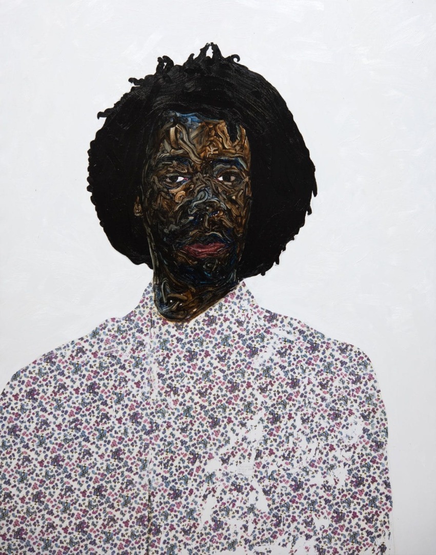 Portrait of a person with textured, curly hair wearing a patterned shirt on a plain background.