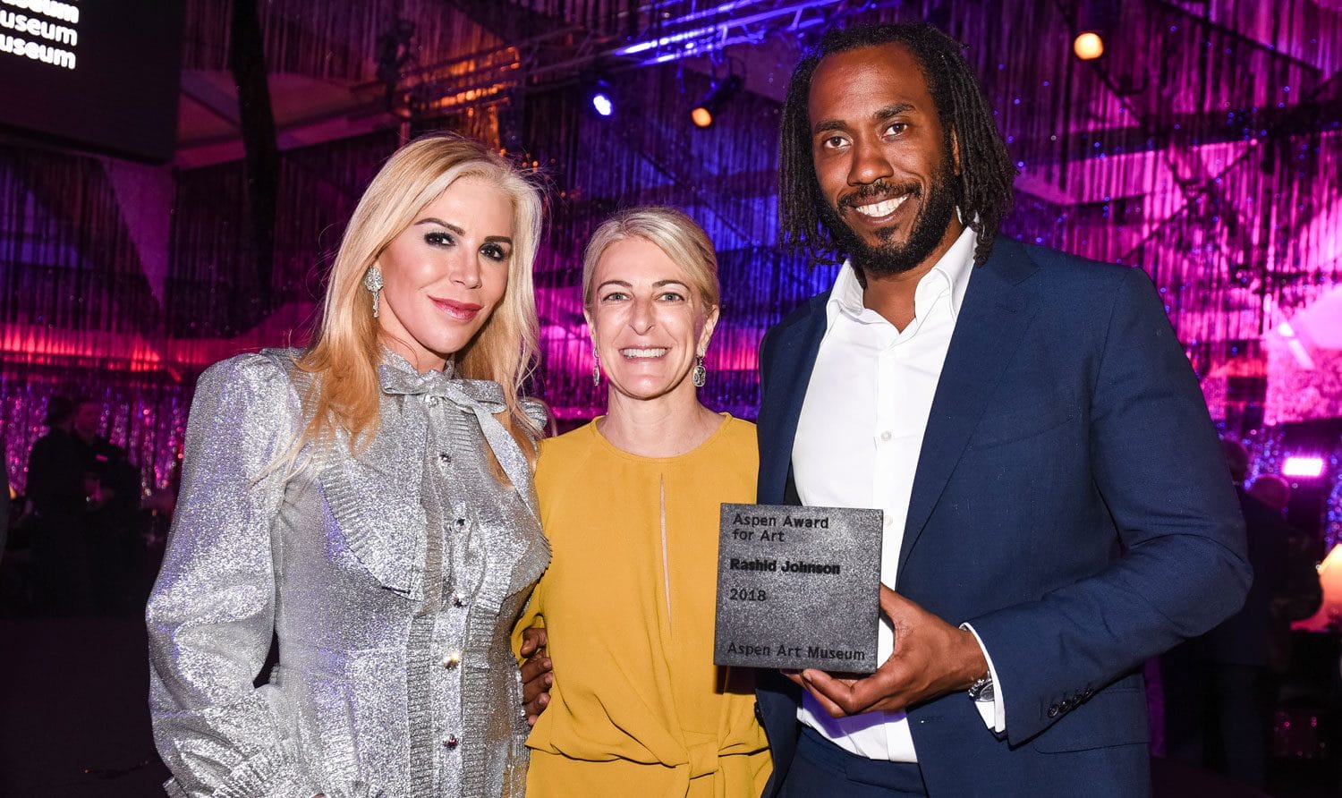 Three people posing together at an art award event, with one holding a plaque.