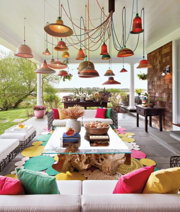 Colorful patio with vibrant hanging lights, eclectic cushions, and lush greenery in background creating a lively outdoor space.