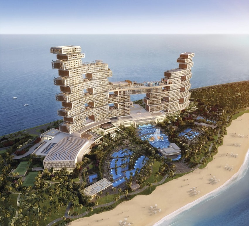 Aerial view of a luxurious beachfront resort with modern architecture, multiple pools, and lush greenery along the shoreline.