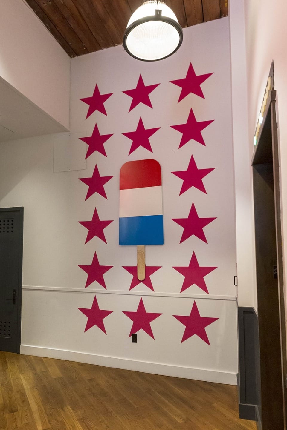 Patriotic red, white, and blue popsicle mural with surrounding red stars on a white wall indoors.