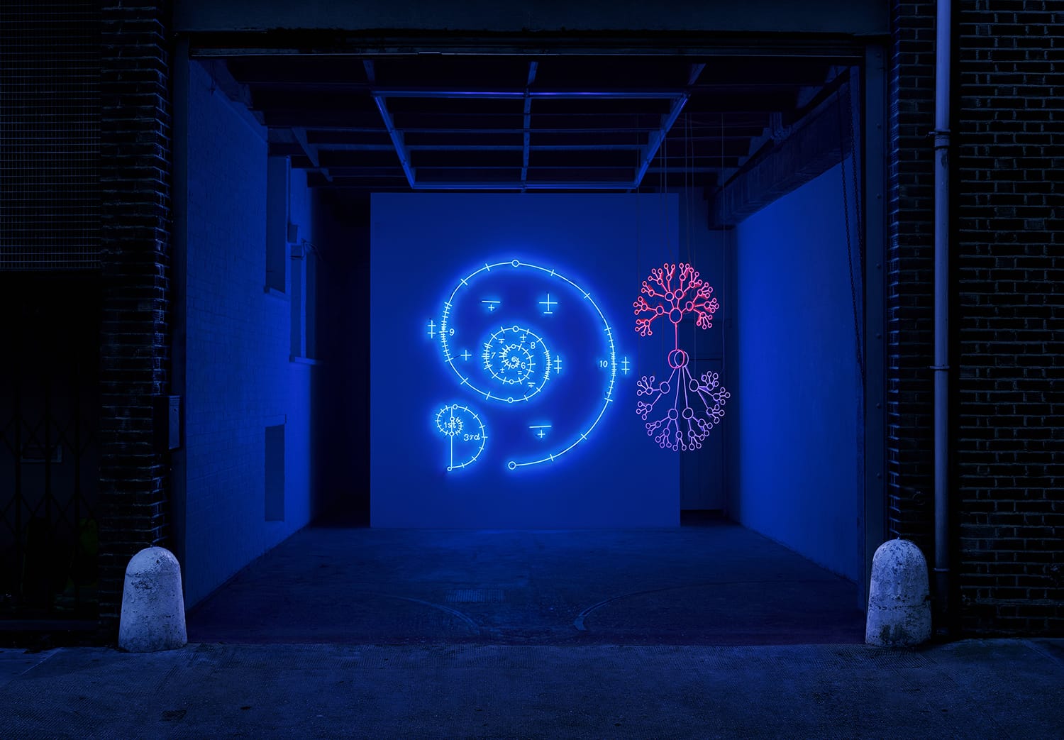 Blue and pink neon spirals and patterns illuminated in a dimly lit room with brick walls and a dark ceiling.