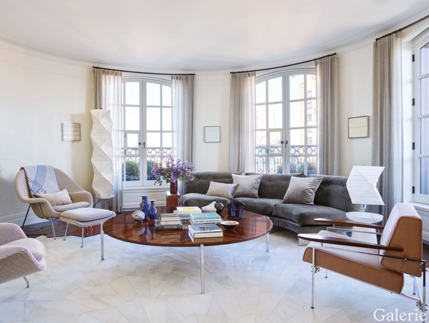 Elegant living room with large windows, modern furniture, a curved sofa, and a coffee table. Soft lighting enhances the cozy atmosphere.