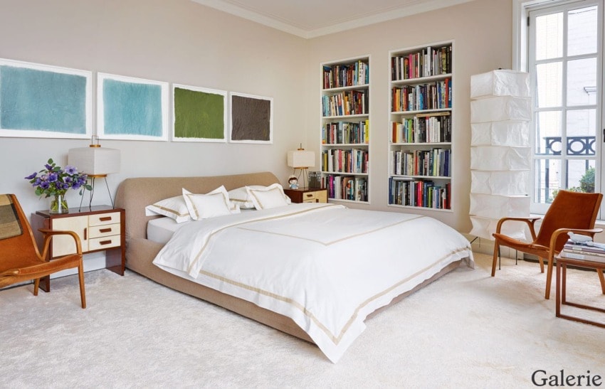 Modern bedroom with a beige bed, colorful artwork, bookshelf, and elegant decor.