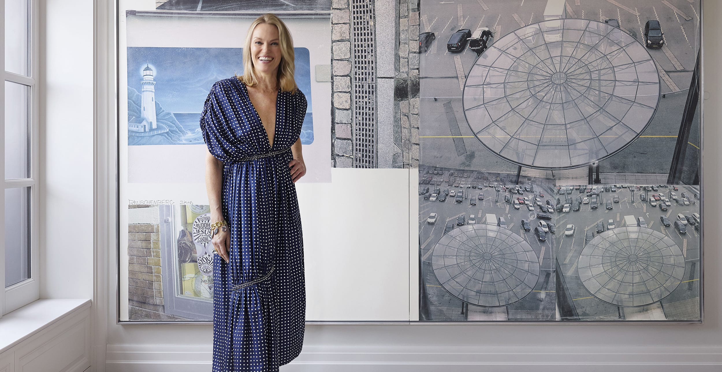 Person in a blue polka dot dress standing by a large artwork featuring urban and architectural imagery.