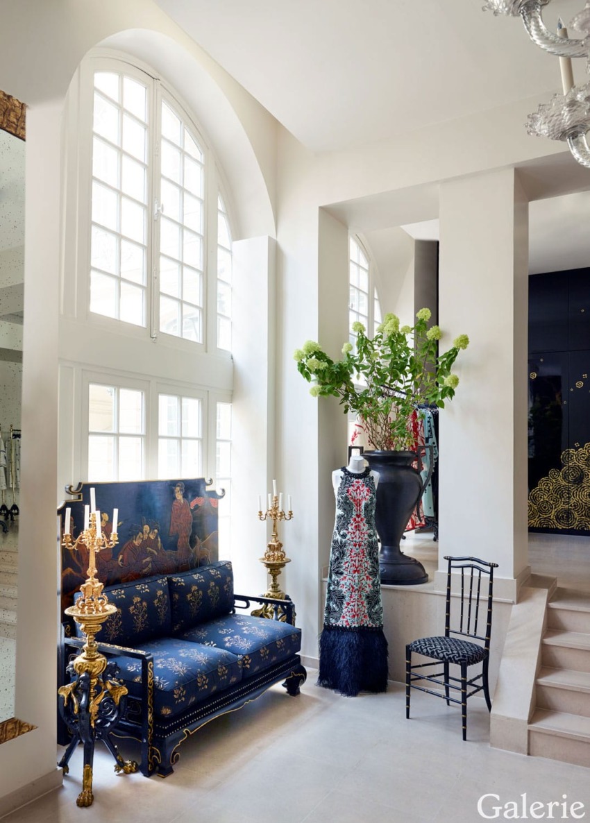 Elegant interior with a blue and gold sofa, decorative mannequin, and large windows letting in natural light.
