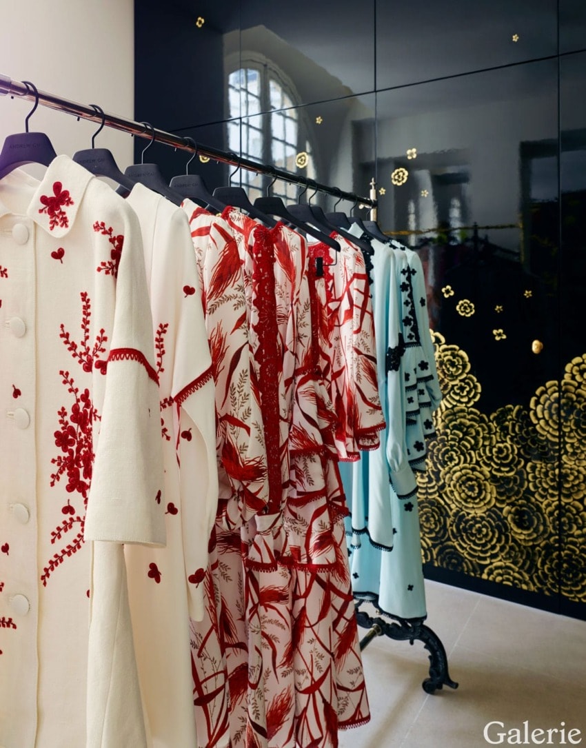 Elegant designer clothing with red and blue patterns hangs in a modern boutique with dark floral decor.
