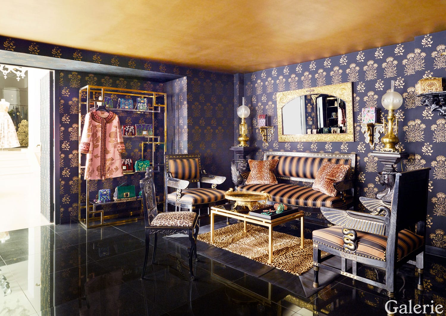 Luxurious living room with elegant wallpaper, striped furniture, gold accents, and a glass display shelf.