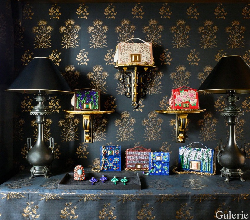 Luxury designer handbags and ornate jewelry displayed on decorated shelves with matching wallpaper and black lamps.