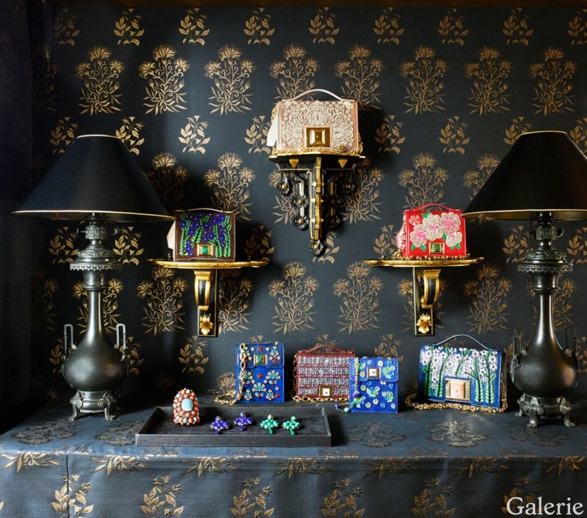 Luxury designer handbags and ornate jewelry displayed on decorated shelves with matching wallpaper and black lamps.