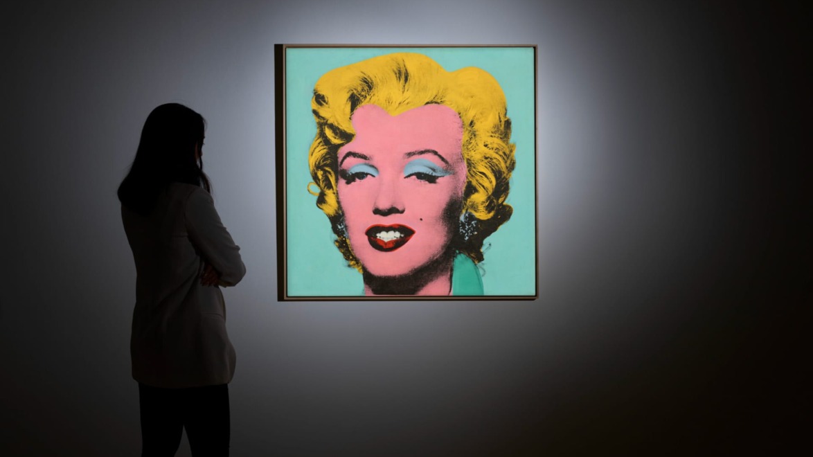 Person looking at a vibrant pop art portrait of a woman with yellow hair on a green background in a dimly lit room