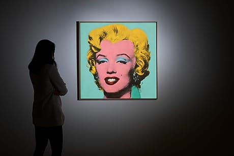 Person looking at a vibrant pop art portrait of a woman with yellow hair on a green background in a dimly lit room