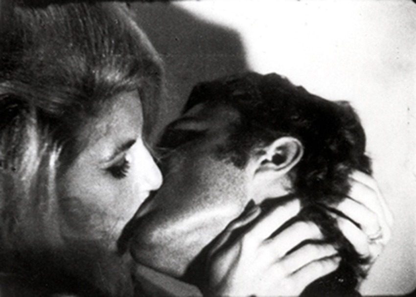 A black and white photo of a couple sharing an intimate kiss with their hands gently touching each other's faces.
