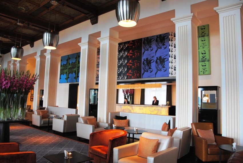 Hotel lobby with modern decor, vibrant artwork, and comfortable seating areas featuring armchairs and side tables.