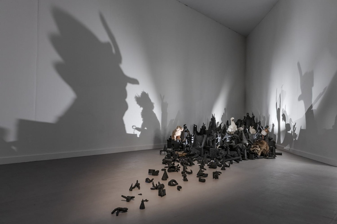 Art installation with various objects casting intricate shadows on a gallery wall, creating abstract shapes and figures.