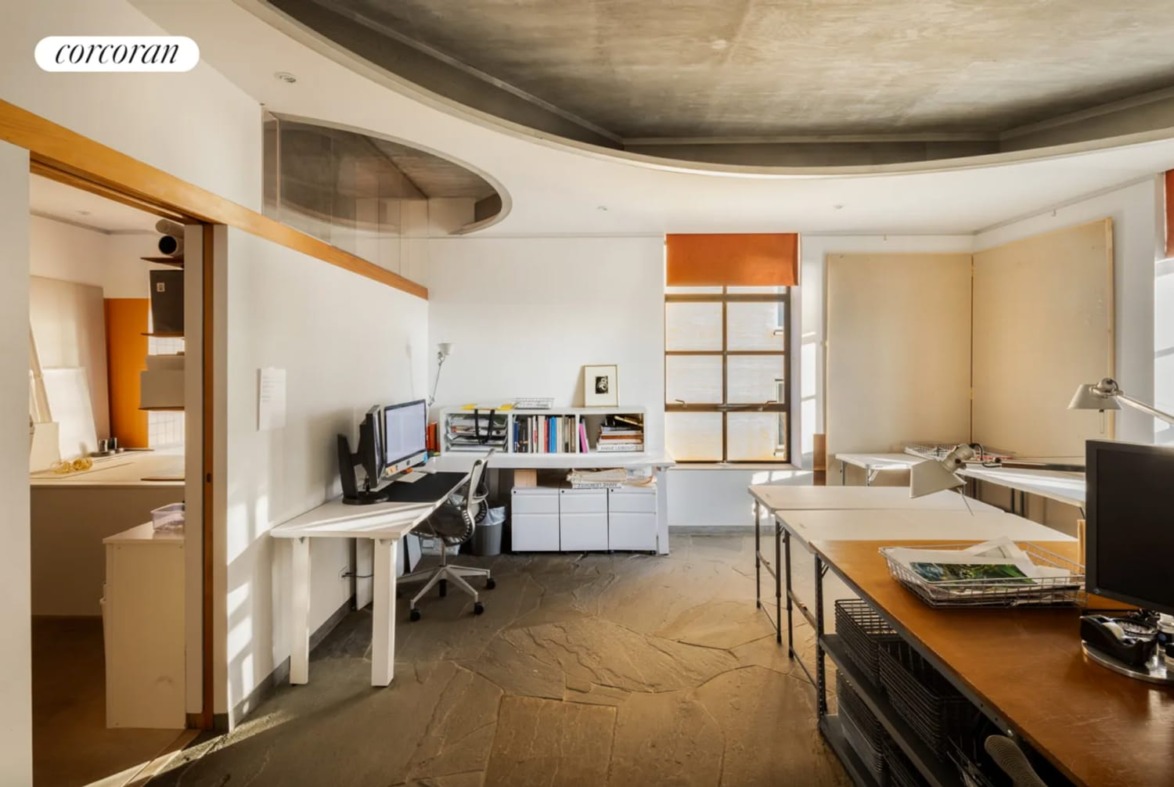 Modern office space with computers, desks, natural light from windows, and a unique curved ceiling design.