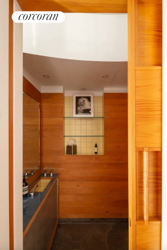 Modern bathroom with wooden panels, double sink, mirrored wall, and decorative photo on shelf above yellow-tiled backsplash.