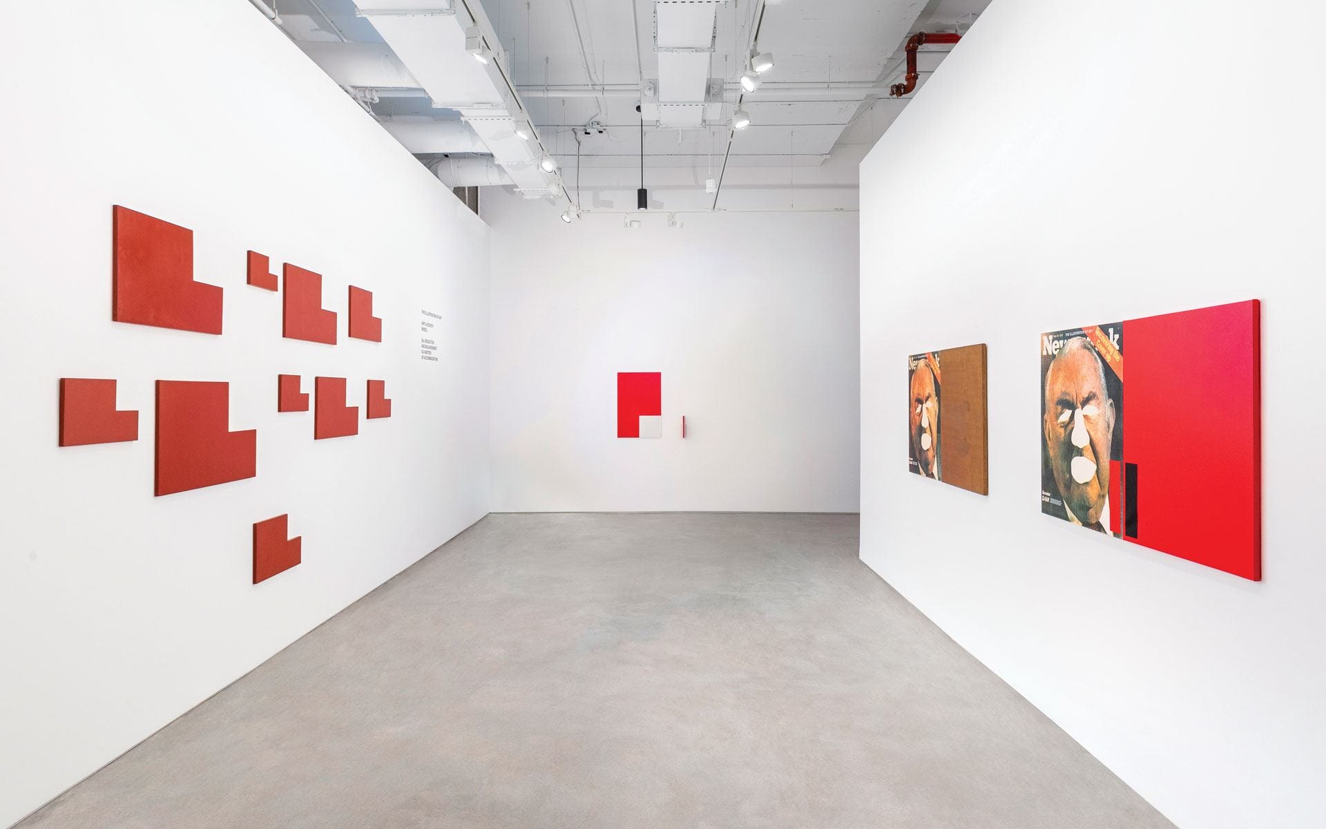 Art gallery with abstract red and brown paintings on white walls, geometric designs displayed on the left wall.