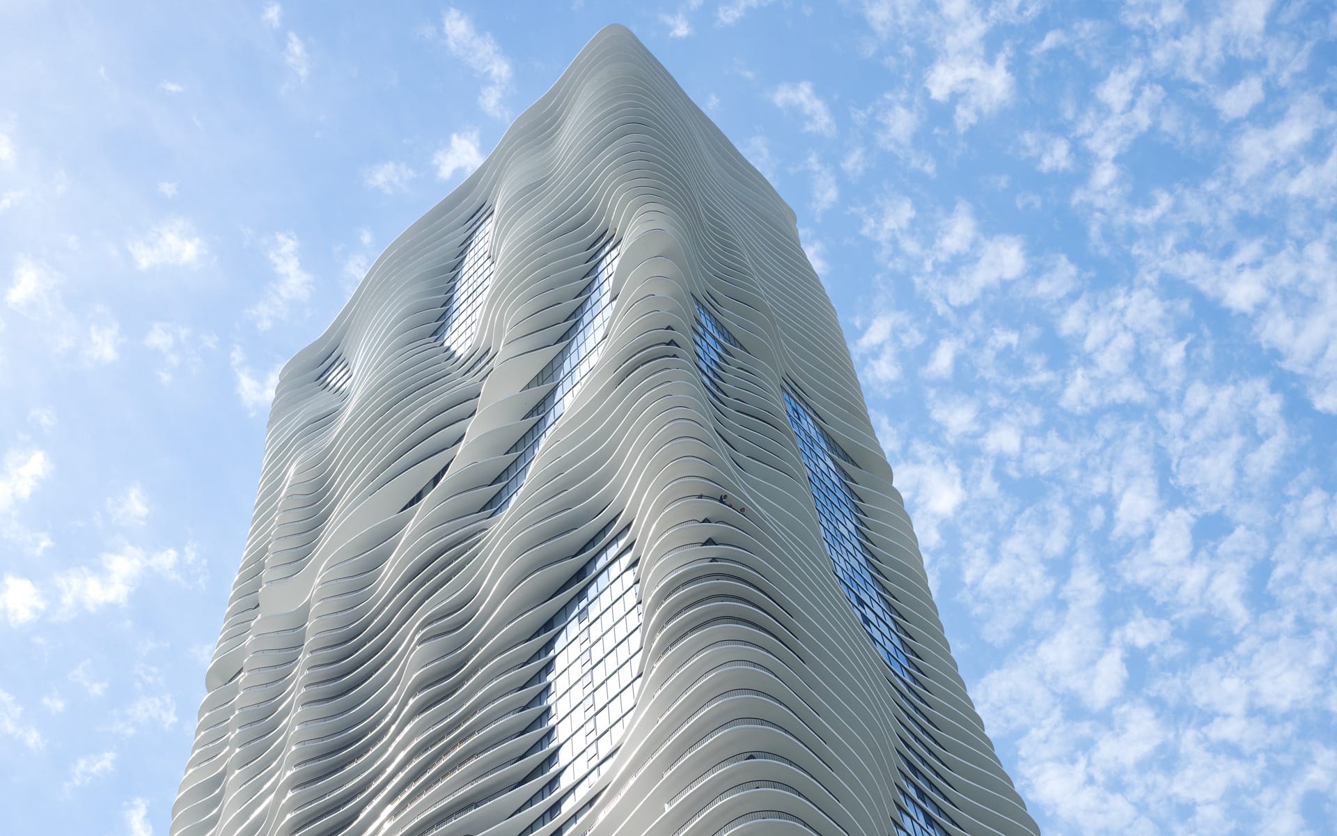 Curved skyscraper with wave-like design against a blue sky with scattered clouds