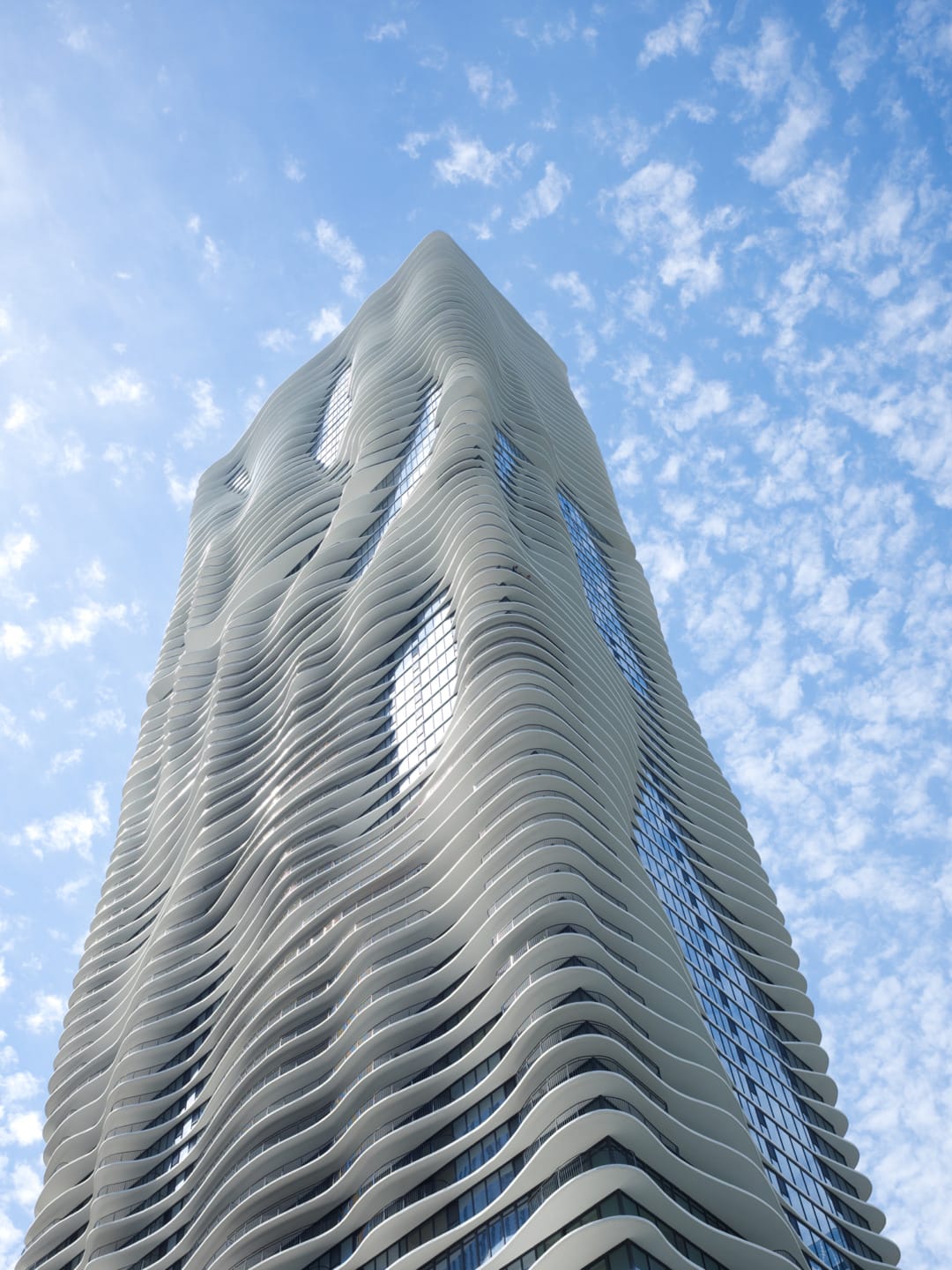 Modern skyscraper with wavy, undulating design against a blue sky with scattered clouds.